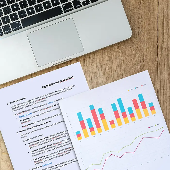 Laptop with SmarterMail documentation and analytics report showing bar and line charts